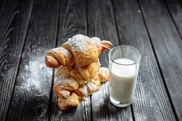 three croissants with glass of milk on dark wooden background close-up top view
