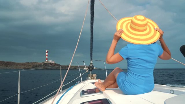 Woman in a yellow hat and blue dress girl rests aboard a yacht on summer season at ocean