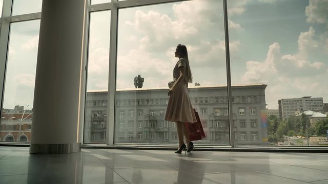 Silhouette of young attractive girl goes to window in mall, holds bags, shopping concept, fashion concept