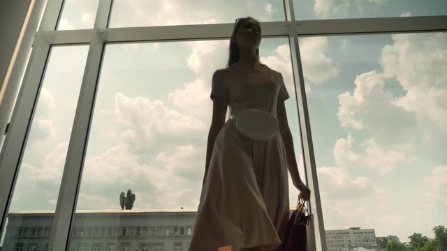 Silhouette of young attractive girl goes to window in mall, holds bags, shopping concept, fashion concept, bottom view