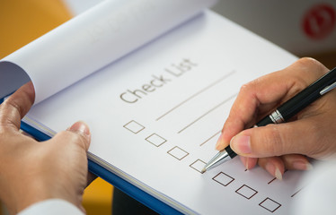 Close- up hand holding pen on check list paper and the format for filling in information in...