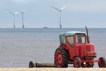 The future of energy production. Red diesel tractor in front of distant offshore sustainable resource wind turbines
