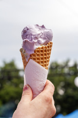 Female hand holds a cone of soft milk ice cream in a waffle cup against the sky