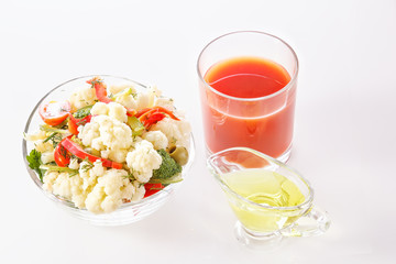 Fresh salad of cauliflower with tomato, broccoli, olives, sweet pepper, greens with a glass of tomato juice and a glass nipple on a white background