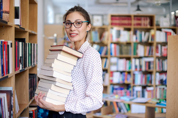 Young woman with a stack of books in library