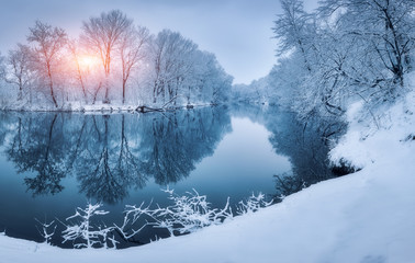 Winter forest on the river at sunset. Colorful landscape with snowy trees, frozen river with reflection in water. Seasonal. Snow covered trees, lake, sun and blue sky. Beautiful forest in snowy winter - Powered by Adobe