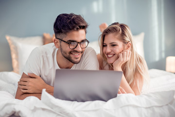 Young couple with laptop in the bed.