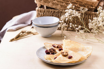 Homemade gluten free rice crepes or pancakes served with dried cranberries and walnuts on wooden table. Healthy breakfast