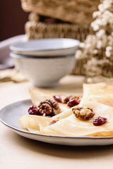 Homemade gluten free rice crepes or pancakes served with dried cranberries and walnuts on wooden table. Healthy breakfast