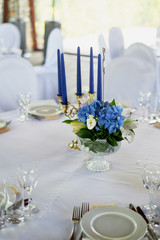 Table with a classic design. With a composition in a high vase with hydrangeas and lilies, a Golden candlestick with blue candles. Decor and floristry