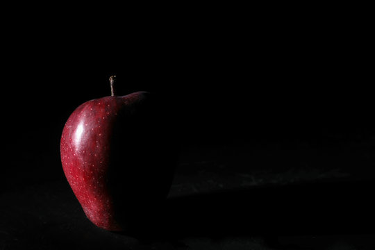 A red apple with black background with one sided light