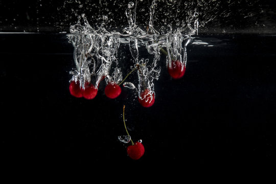 Plum red cherries splashing in water