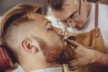 Man in the process of trimming a beard in a barbershop.  Photo in vintage style