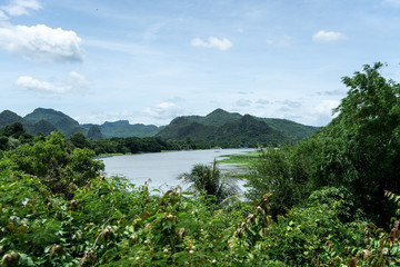 Fototapeta na wymiar View of river Kwai with mountains and tropical forest and in background and trees in the foreground during a bright sunny day, Kanchanaburi, Thailand