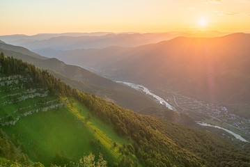 the morning sun illuminates the green slopes of the mountains in summer with the river flowing down the gorge