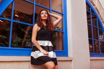 Happy young woman sitting against blue window. Outdoor portrait of beautiful middle eastern girl smiling