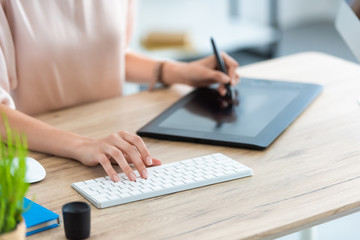 cropped image of female freelancer drawing on graphic tablet at table with computer in home office