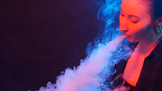 Young woman smoke an electronic cigarette. Smoking in color light
