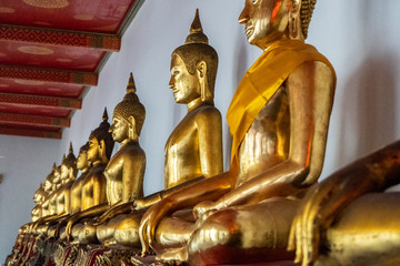 Traditional Thai golden sitting buddha statues aligned in row, Wat Pho, Bangkok, Thailand