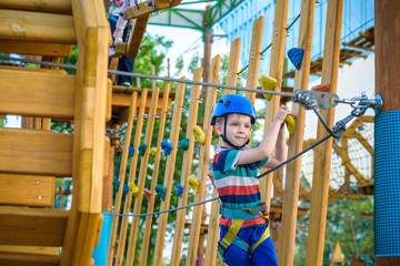 boy having fun at adventure park. toddler climbing in a rope playground structure.