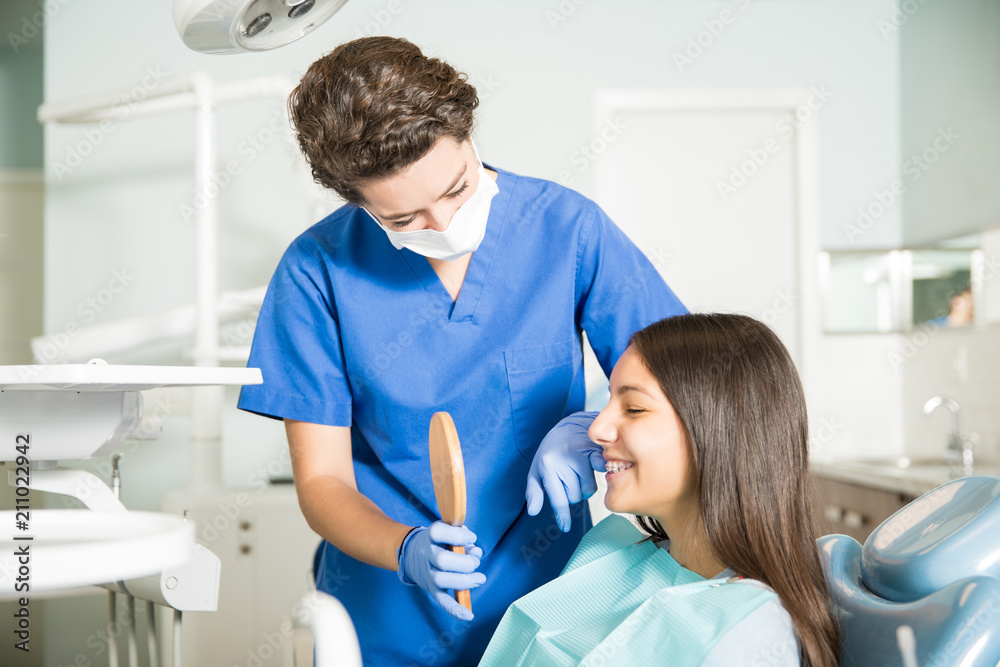 Wall mural dentist showing mirror to teenage girl in clinic