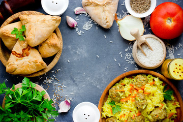 Traditional caucasian food and ingredients on table top view: delicious rice meatballs pilaf, samosa patties with meat, spices, greens