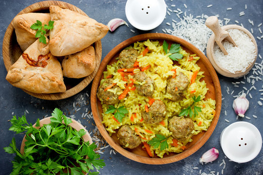 Traditional caucasian food and ingredients on table top view: delicious rice meatballs pilaf, samosa patties with meat, spices, greens