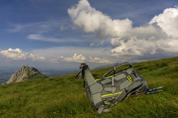 Backpack on green grass against the background of mountains and sky.