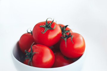 Red tomatoes in a white bowl on white background