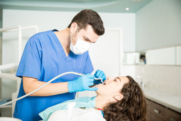Obraz na płótnie Canvas Woman Receiving Dental Treatment From Dentist In Clinic