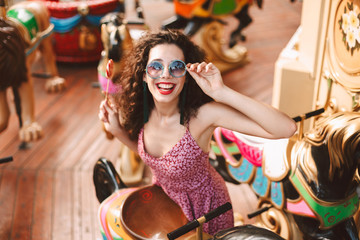 Smiling lady with dark curly hair in sunglasses and dress standing with lolly pop candy in hand and...