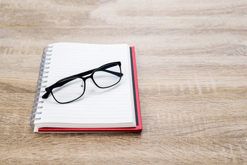Concept Education or business  : Open diary  or note book with black glasses on wooden table.