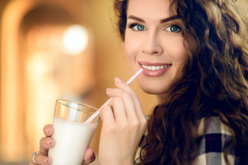 Attractive young woman in plaid shirt and curly hair drinks milkshake in summer in the park