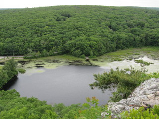 View over the edge of a cliff on a mountain on Lantern Hill trail in Connecticut, with a pond below in the distance 