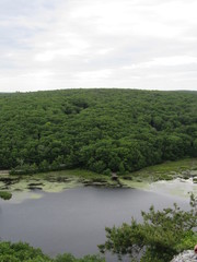 Fototapeta premium View over the edge of a cliff on a mountain on Lantern Hill trail in Connecticut, with a pond below in the distance 