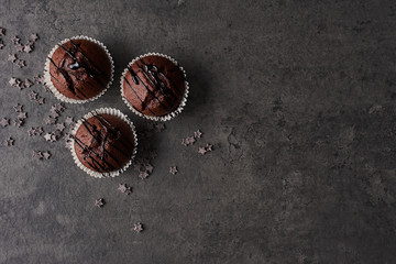 Flat lay of three chocolate muffins topped with chocolate dressing surrounded with chocolate stars...