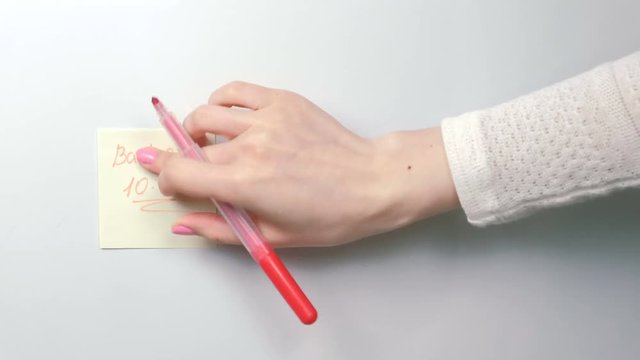 Closeup woman's hands stick yellow sticker paper sheets with words back at 10:00 on a white board.