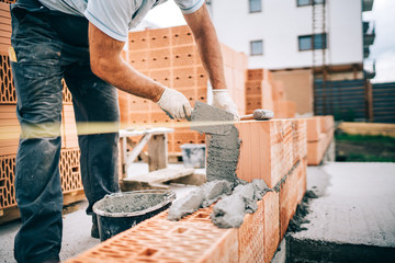 Close up of industrial worker, bricklayer installing bricks on construction site - obrazy, fototapety, plakaty
