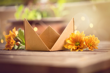 Umweltfreundliches Papierschiffchen auf Holztisch mit orangefarbenen Blüten