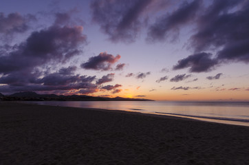 Violet and pink colours of sunrise on the beach. Scattered clouds and sun glow