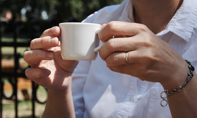 Woman with a ring on her hands holding a white cup of coffee in a garden on a sunny day