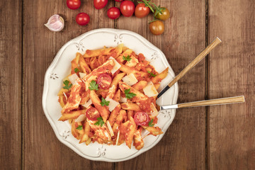Penne pasta with tomato sauce, chicken, and cheese, with fork and spoon plunged into plate
