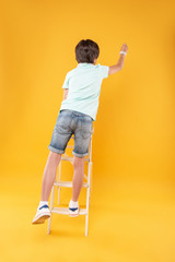 Fototapeta na wymiar Decoration process. Excited slim boy standing on the ladder and sticking pins