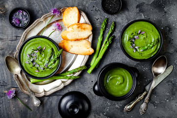 Homemade green spring asparagus cream soup decorated with black sesame seeds and edible chives flowers