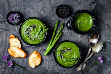 Homemade green spring asparagus cream soup decorated with black sesame seeds and edible chives flowers