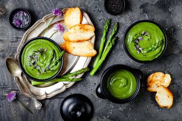 Homemade green spring asparagus cream soup decorated with black sesame seeds and edible chives flowers