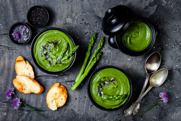 Homemade green spring asparagus cream soup decorated with black sesame seeds and edible chives flowers