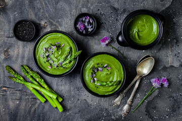 Homemade green spring asparagus cream soup decorated with black sesame seeds and edible chives flowers
