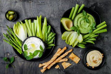 Green vegetables snack board with various dips. Yogurt sauce or labneh, hummus, herb hummus or...