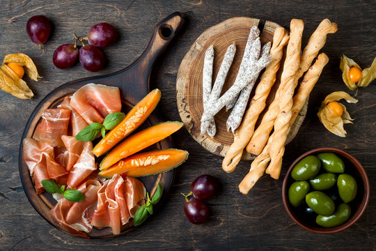 Fototapeta Appetizers table with italian antipasti snacks and wine in glasses. Cheese and charcuterie variety board over rustic wooden background